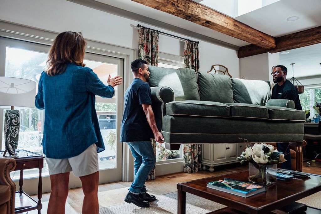 Two LoadUp Loaders lifting a green three-seat sofa out of a Montclair living room while the customer directs them toward the door