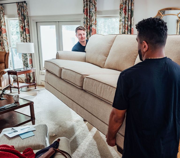 Two LoadUp Loaders lifting a cream sofa together inside a Montecito living room