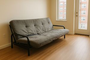 Old gray futon in a small apartment ready for disposal or recycling.