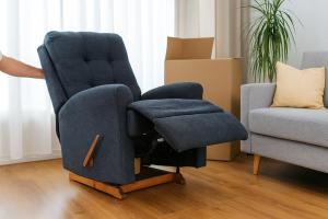 Person moving a large blue recliner chair out of a bright living room during furniture removal.