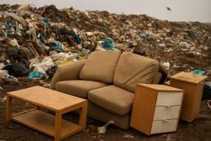 Piles of discarded cheap furniture in a landfill illustrating the environmental impact of fast furniture waste.