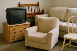 Old furniture including a sofa, armchair, and wooden chair stacked for recycling or donation in a storage area.